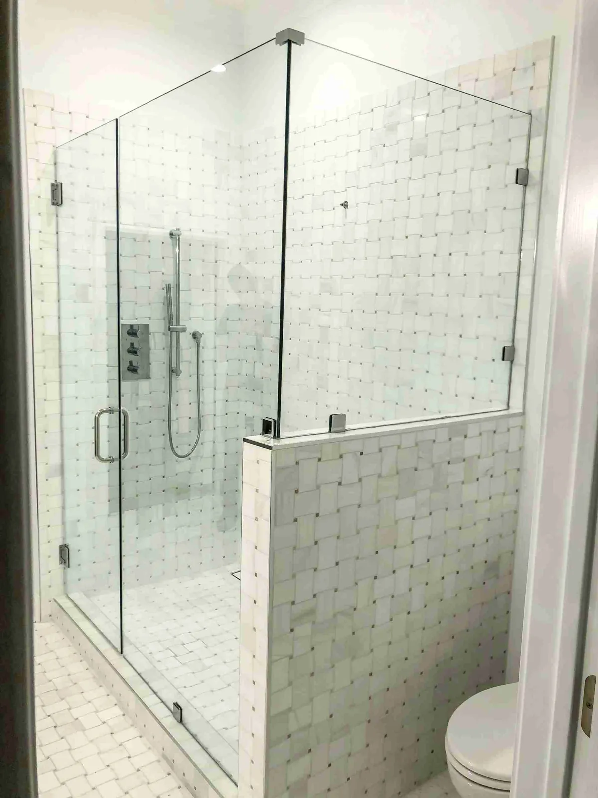 Frameless glass shower door and panels above a marble basketweave tile knee wall
