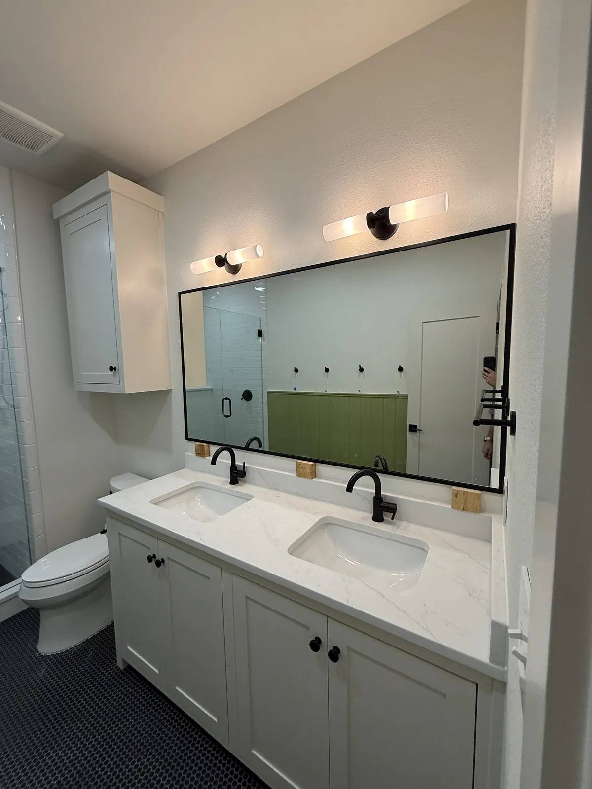 Wide black-framed mirror above a white double vanity with matte black faucets