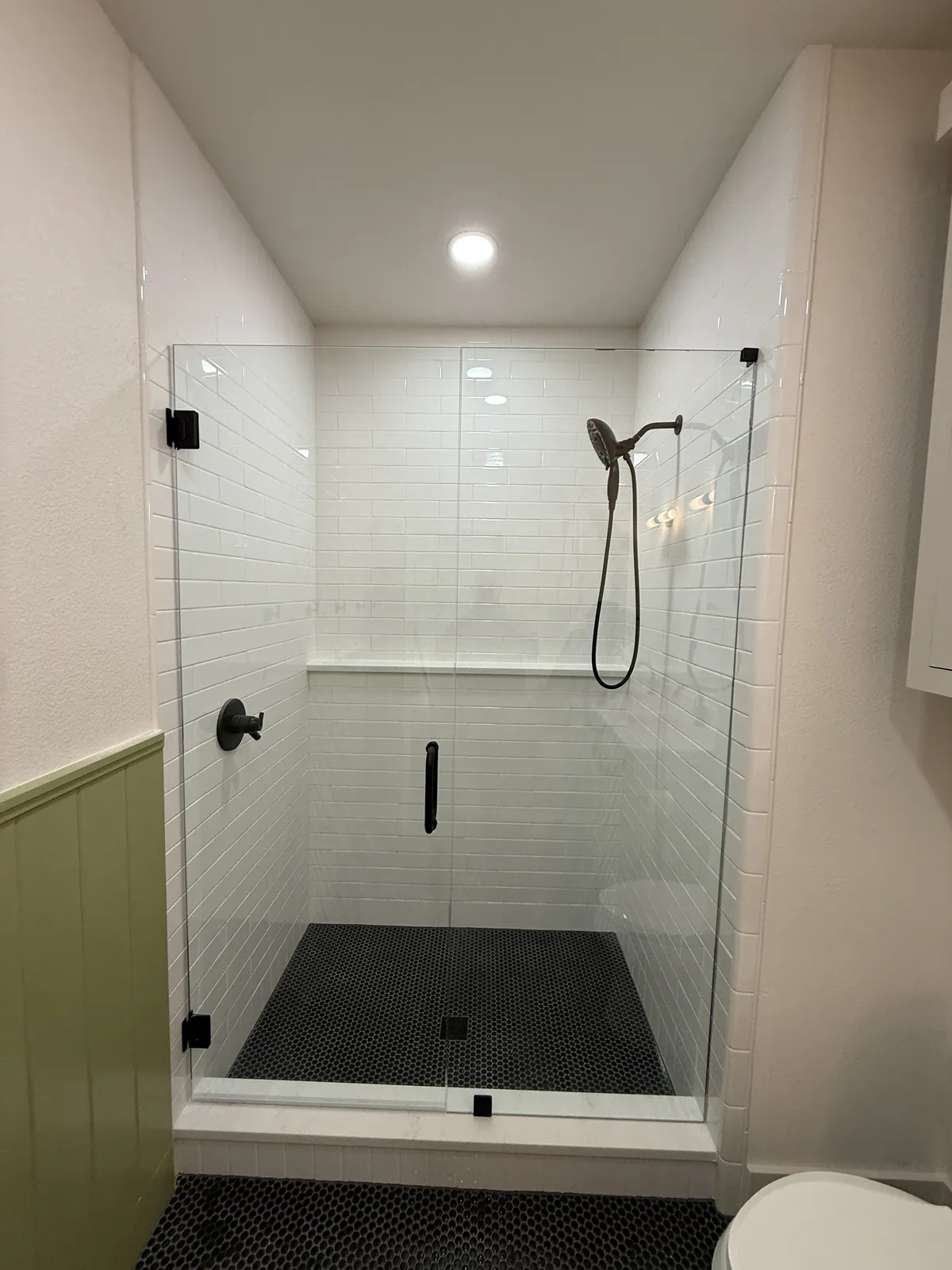 Frameless glass shower door with matte black hinges and pull, white subway tile and a black hex tile floor