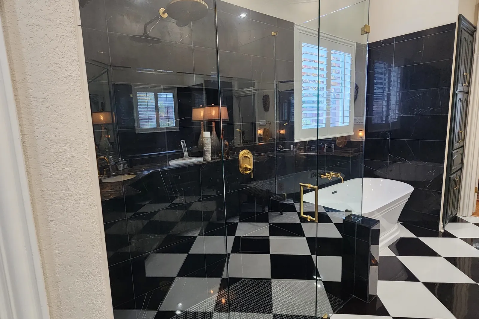 Full-height frameless glass enclosure with brass hinges and handle beside a black and white checkerboard floor