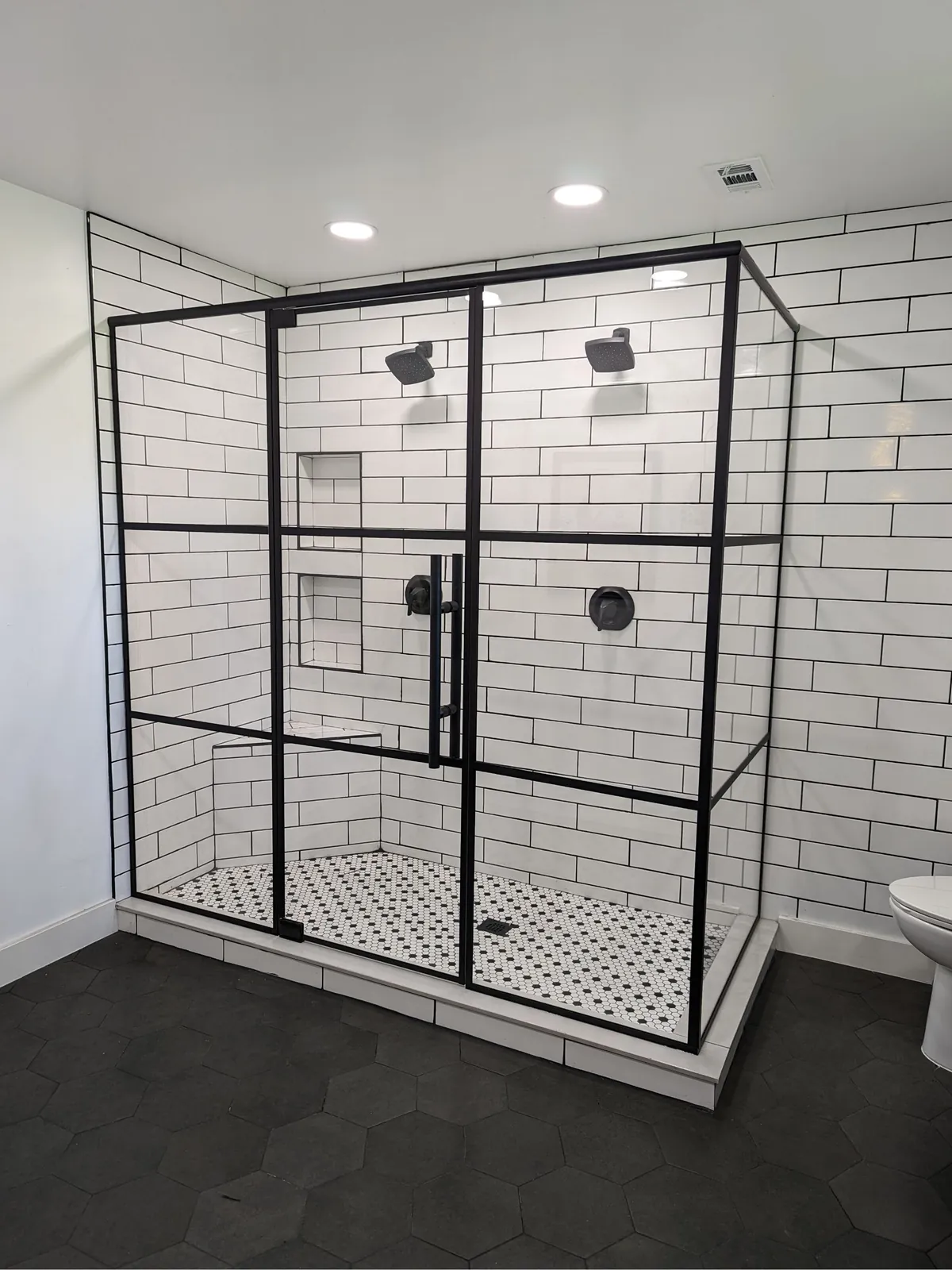 Black grid glass shower enclosure with white subway tile and a black and white mosaic floor