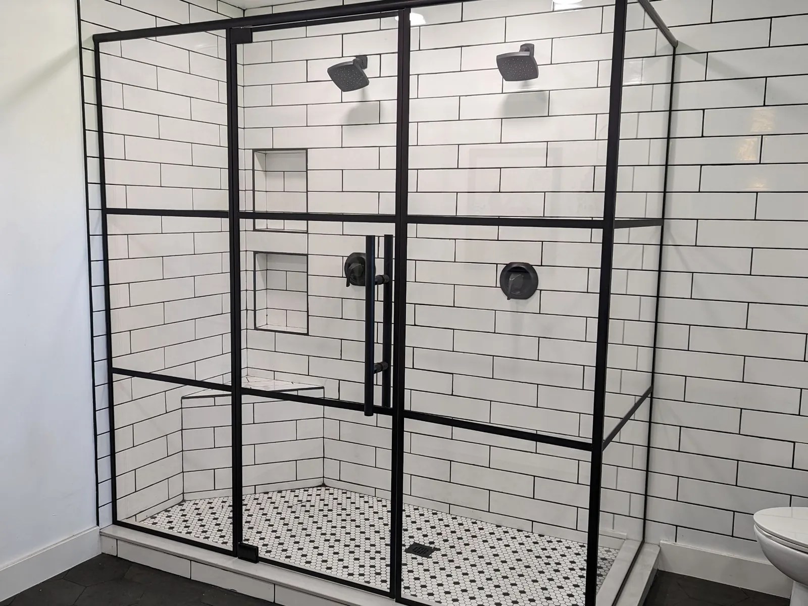 Black grid glass shower enclosure with white subway tile and a black and white mosaic floor