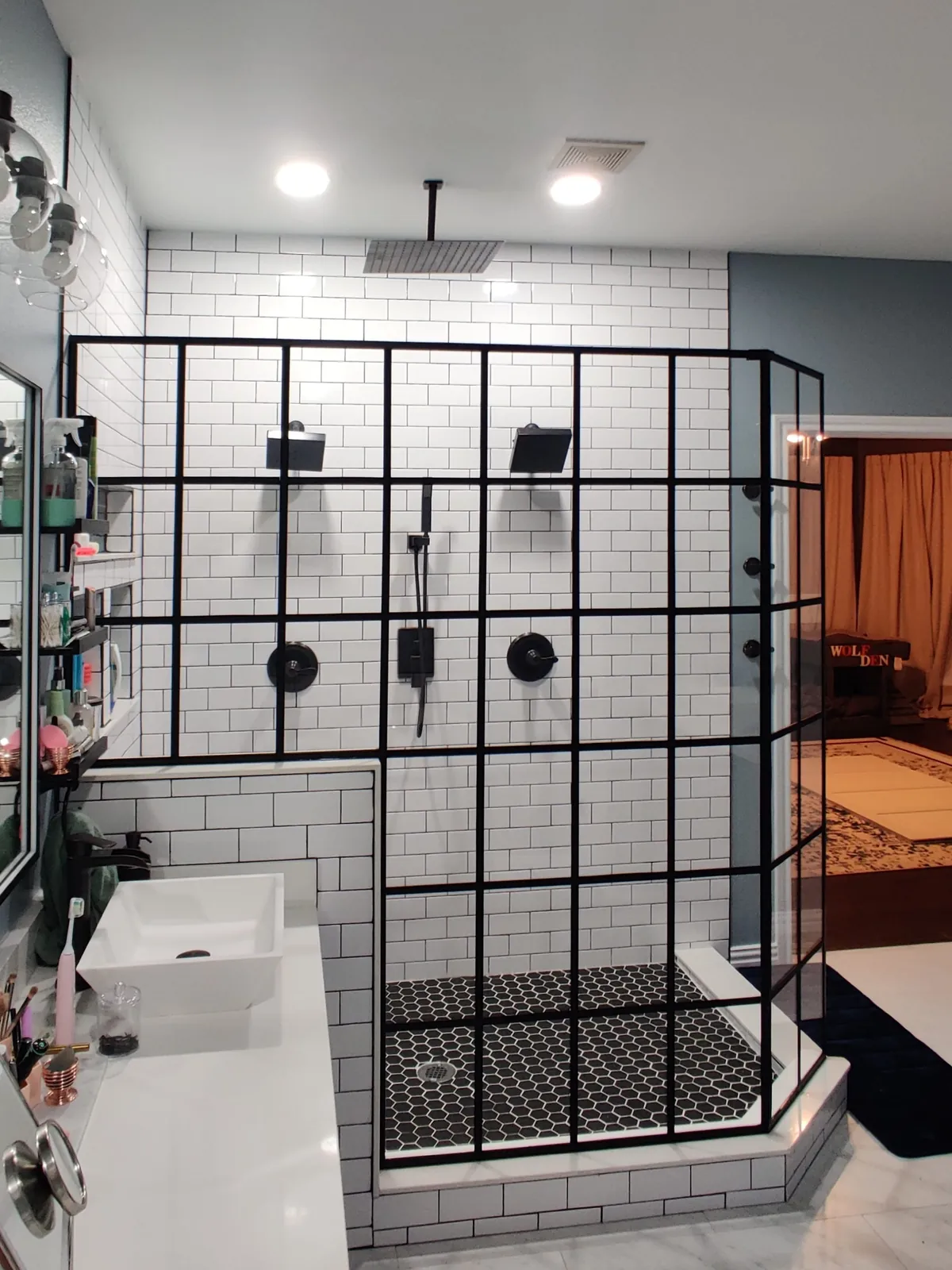Black grid glass shower enclosure with two shower heads and white subway tile