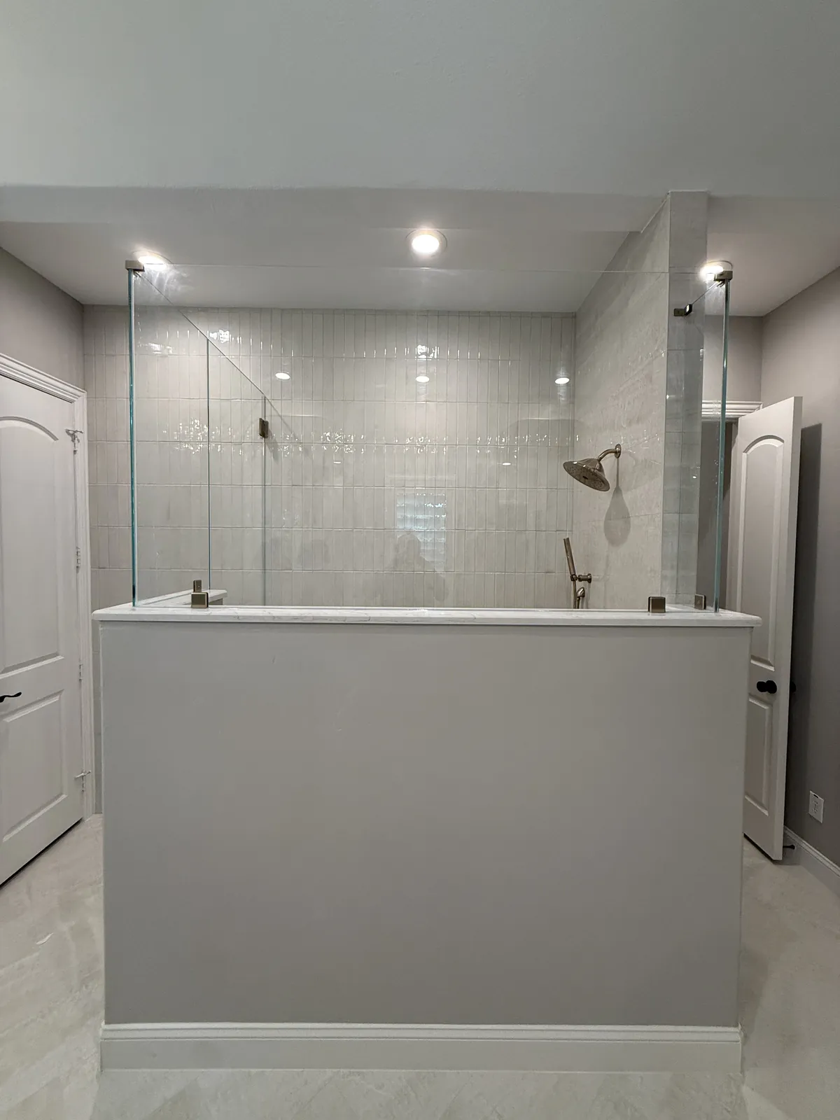 Fixed glass panels on top of a long tiled half wall, with the shower behind