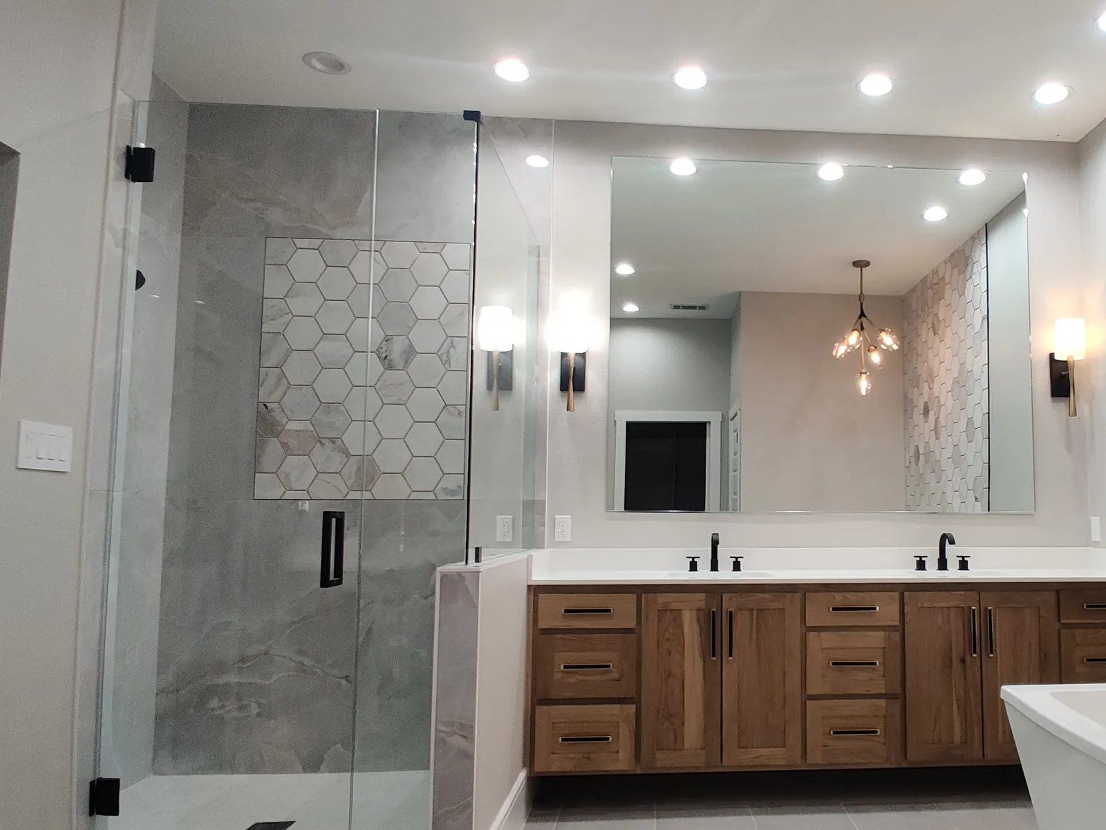 Frameless mirror above a double wood vanity, beside a frameless glass shower