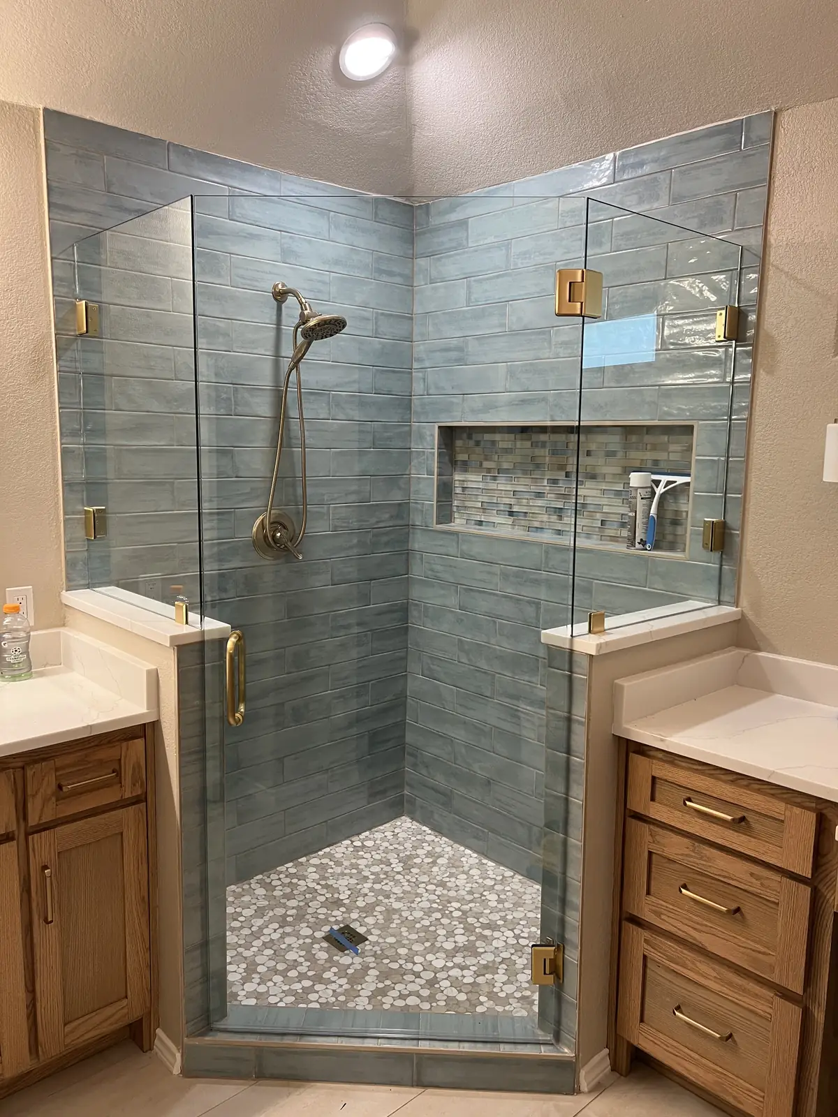 Neo-angle frameless glass shower with brass hinges and blue glazed tile, set between two vanities
