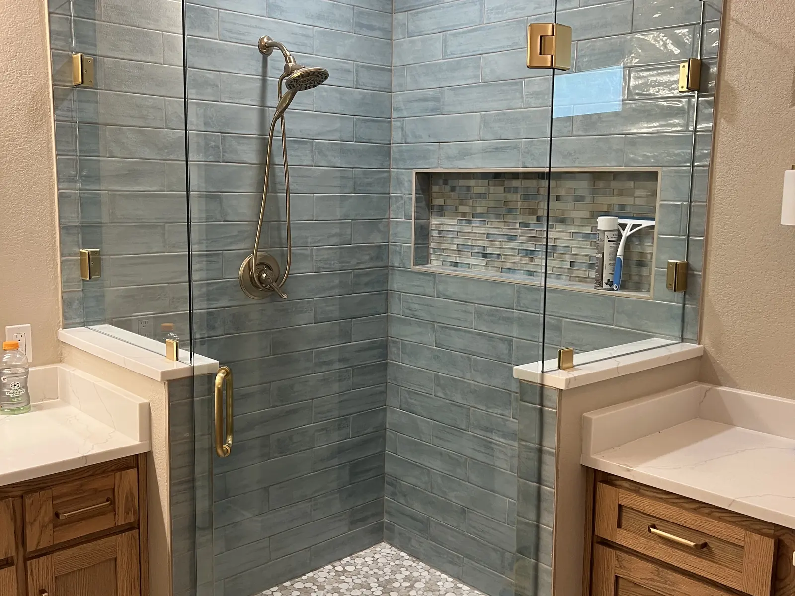Neo-angle frameless glass shower with brass hinges and blue glazed tile, set between two vanities