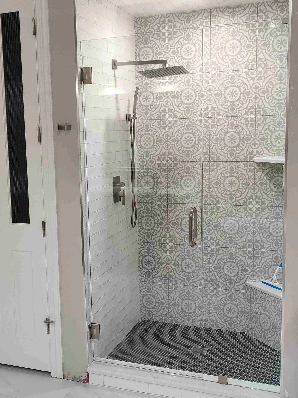 Frameless glass shower door and panel with a brushed nickel pull in front of gray patterned tile