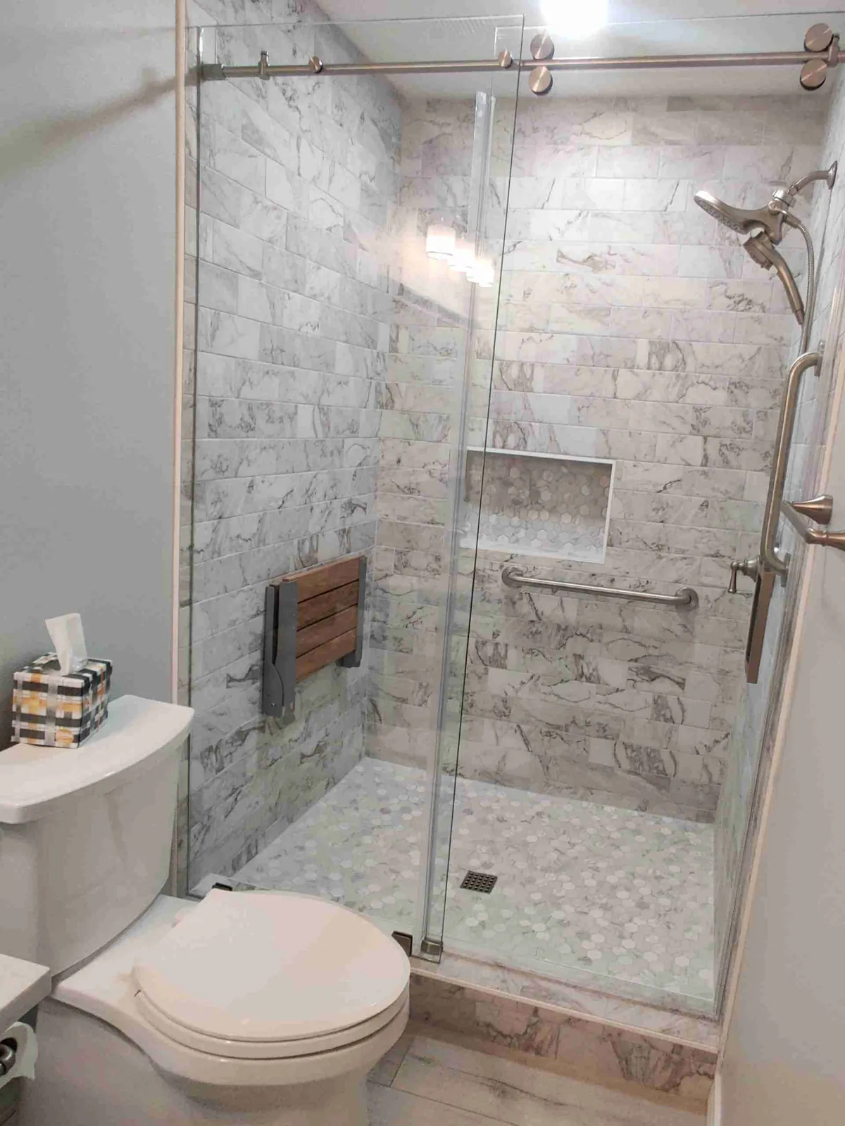 Frameless sliding glass shower door on a brushed nickel roller bar, gray marble-look tile inside