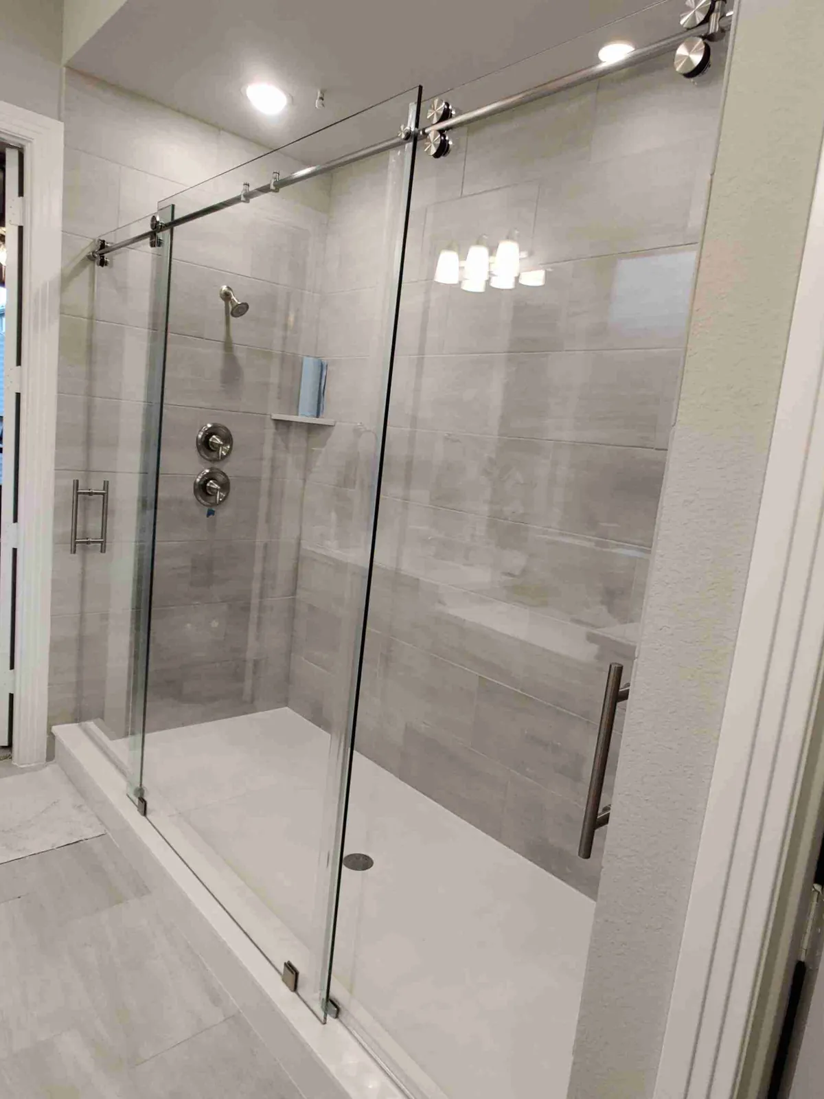 Frameless sliding glass shower door on a chrome roller bar in a gray tile shower