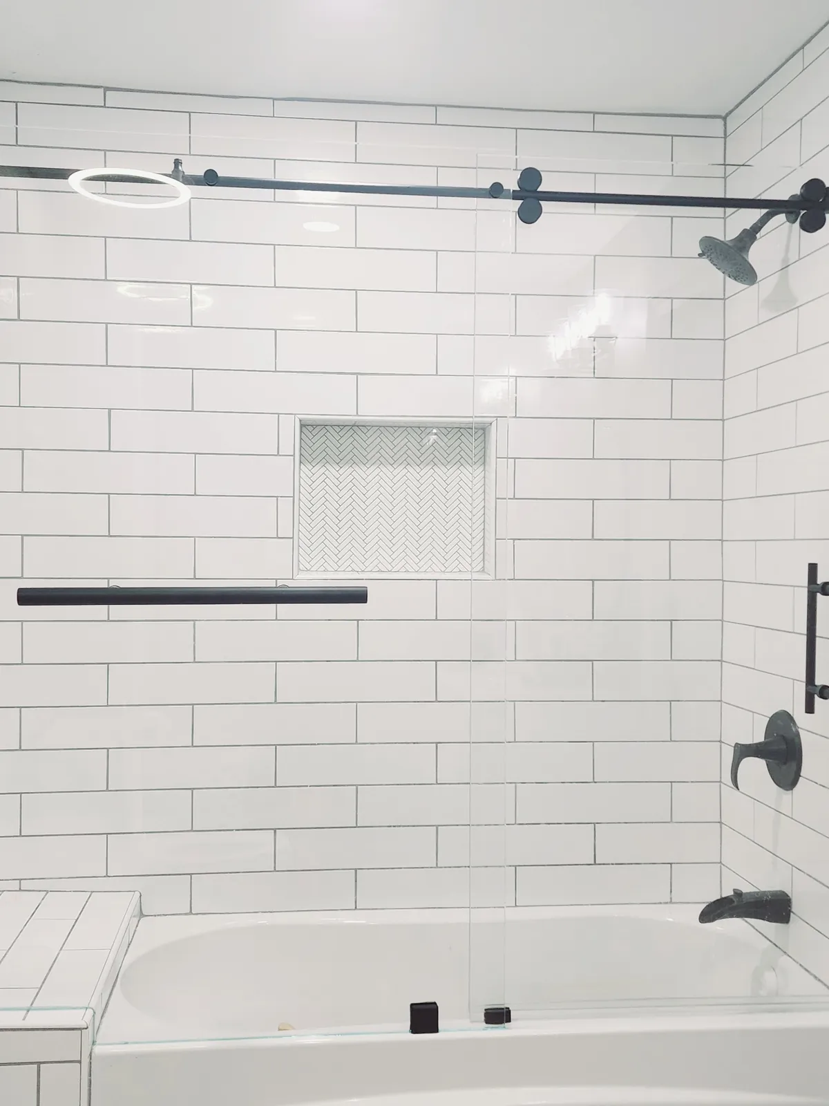 Sliding glass tub door on a matte black roller bar with white subway tile