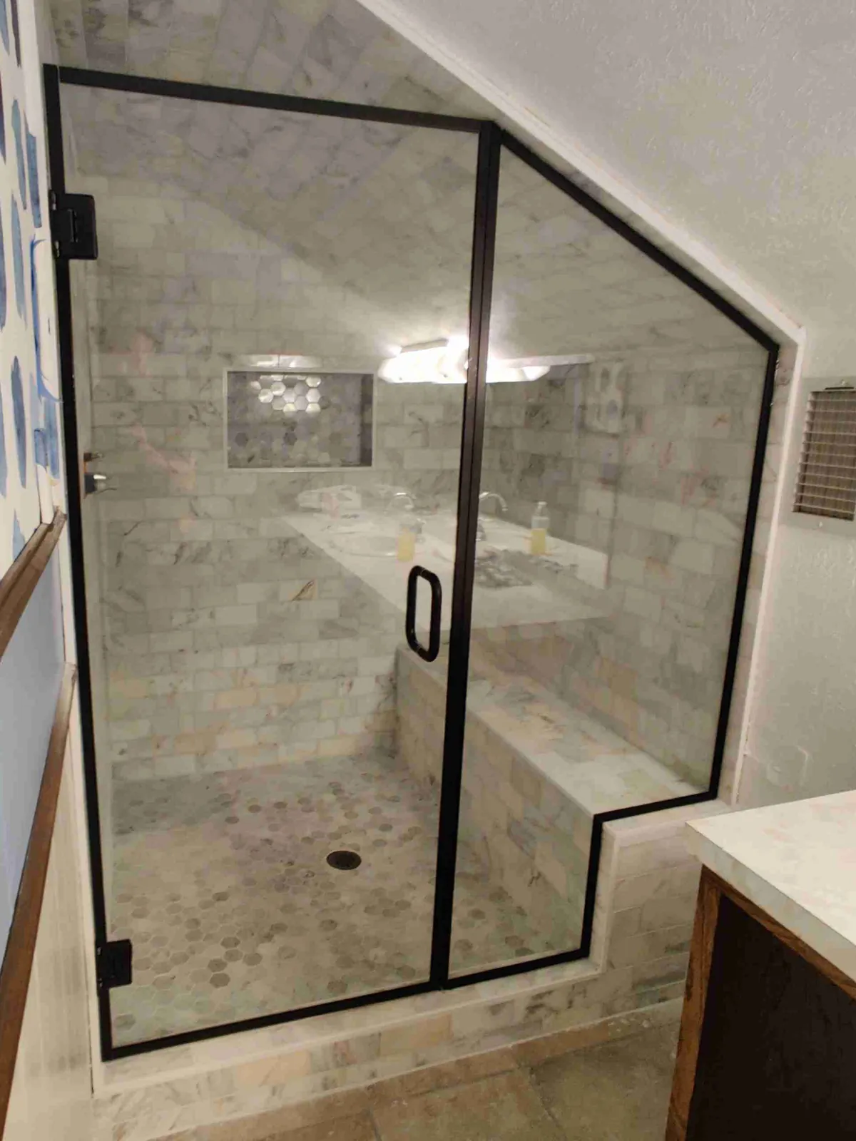 Glass shower door and panels with black trim, cut to follow a sloped ceiling