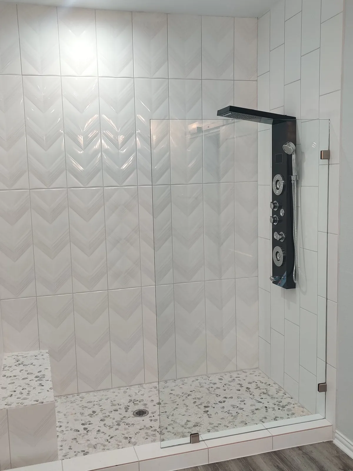Single fixed glass panel on a walk-in shower with white chevron tile and a black shower column