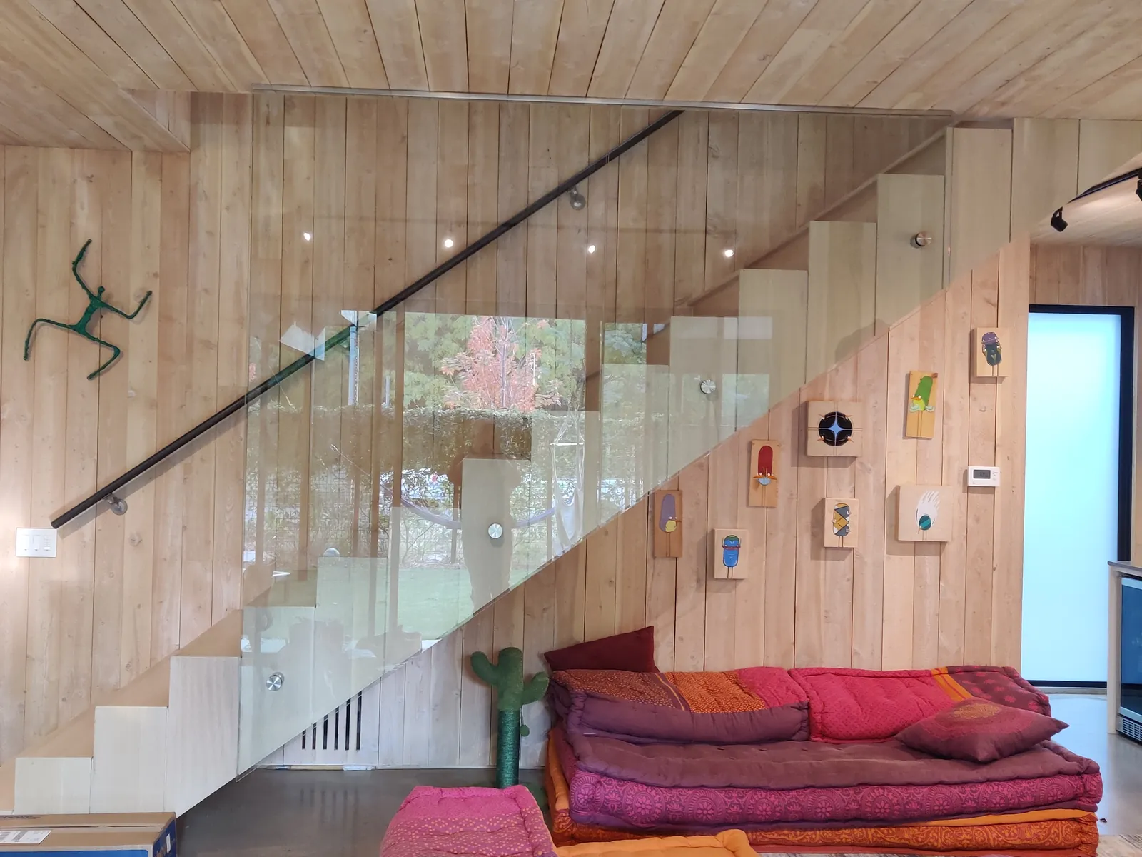Frameless glass stair guard with a black handrail under a wood plank ceiling