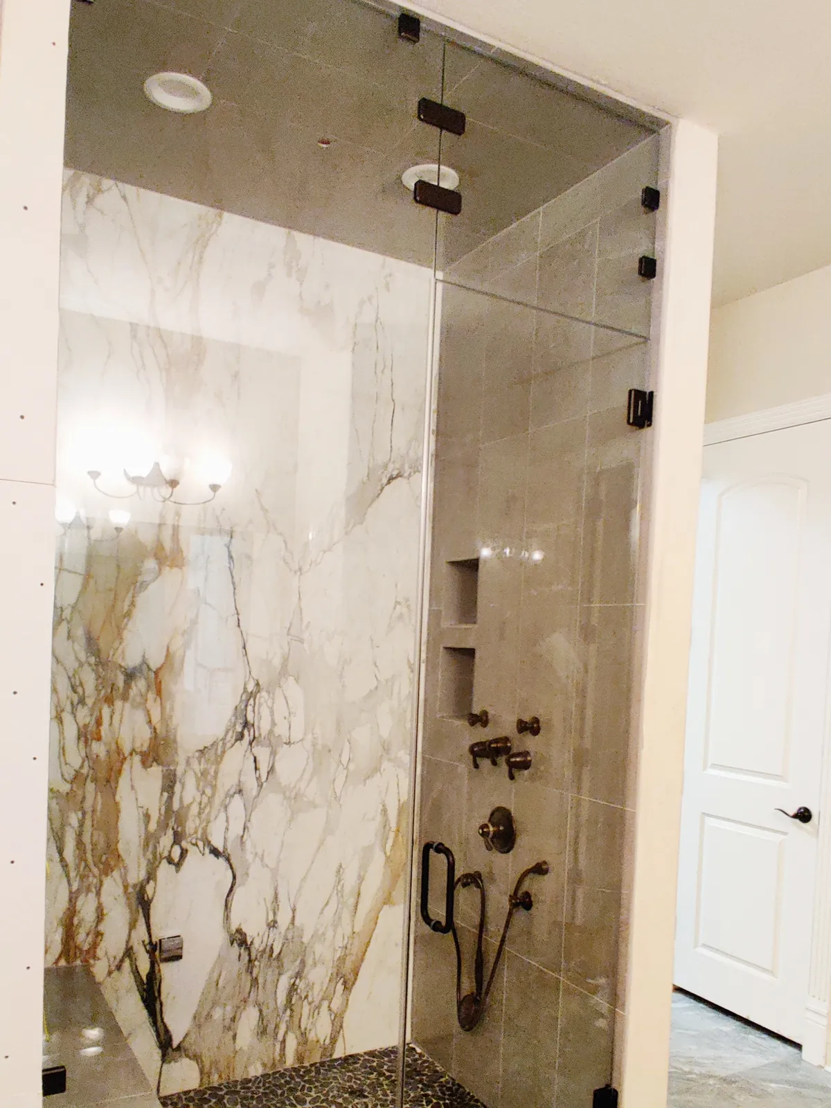 Full-height glass steam shower door and panel with matte black hardware and gold-veined marble walls