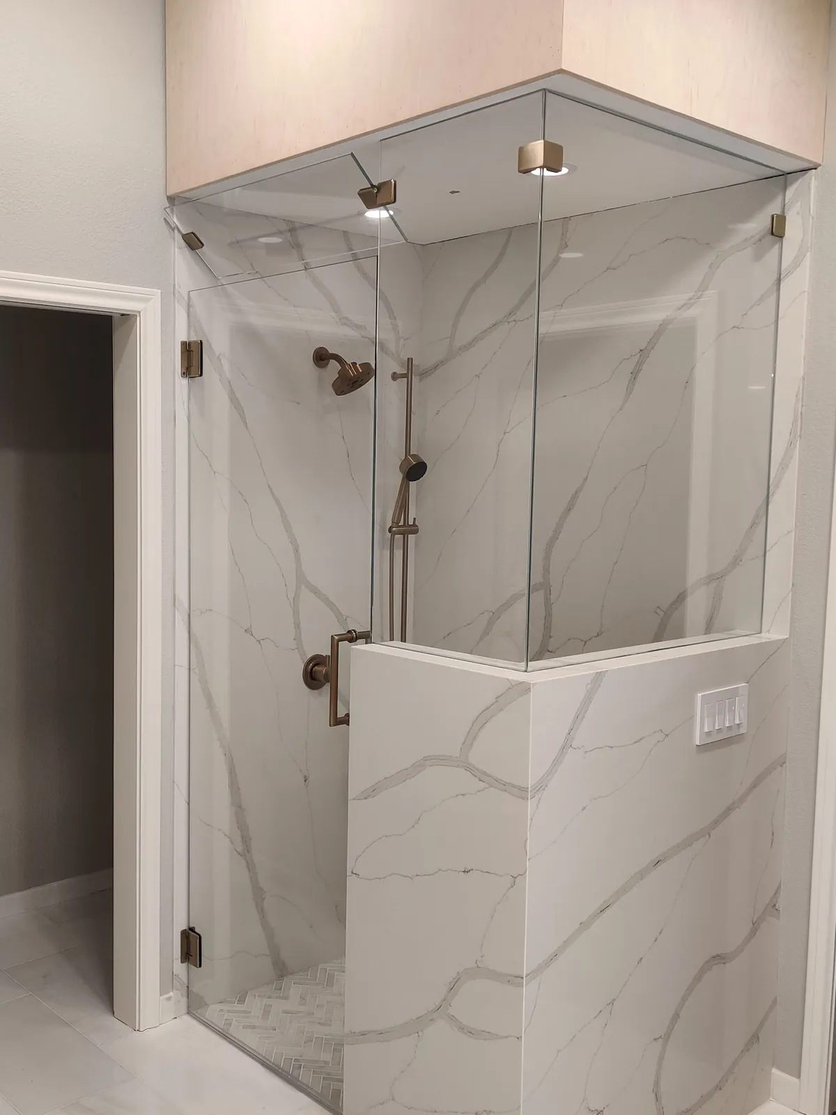 Glass steam shower enclosure with a transom panel to the ceiling, brushed gold hardware and marble-look walls