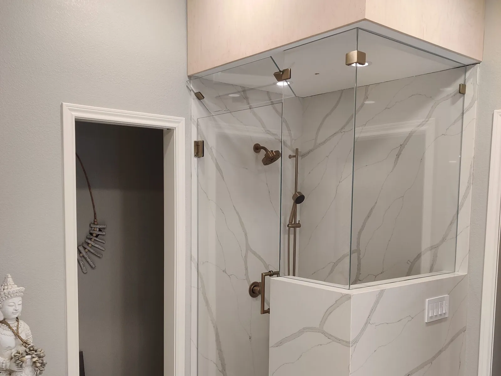 Glass steam shower enclosure with a transom panel to the ceiling, brushed gold hardware and marble-look walls