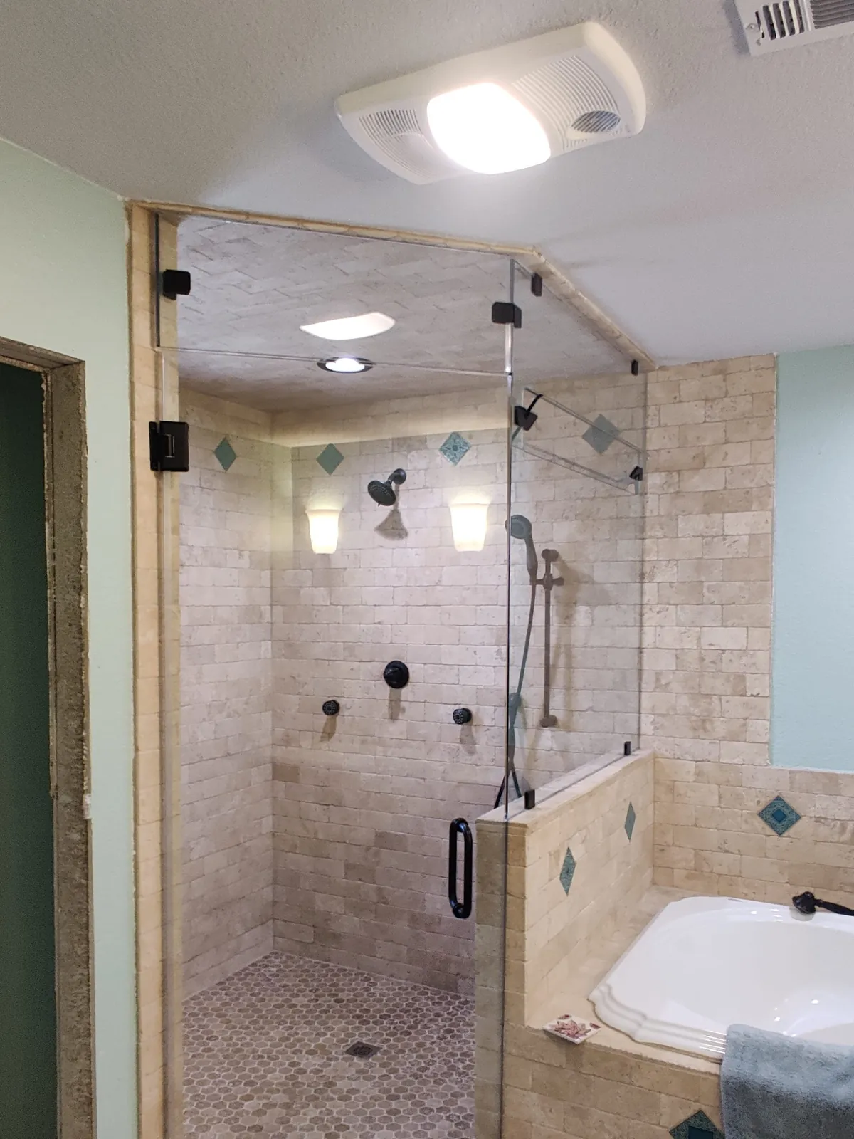 Glass steam shower enclosure with a transom over a tiled knee wall and travertine-look tile