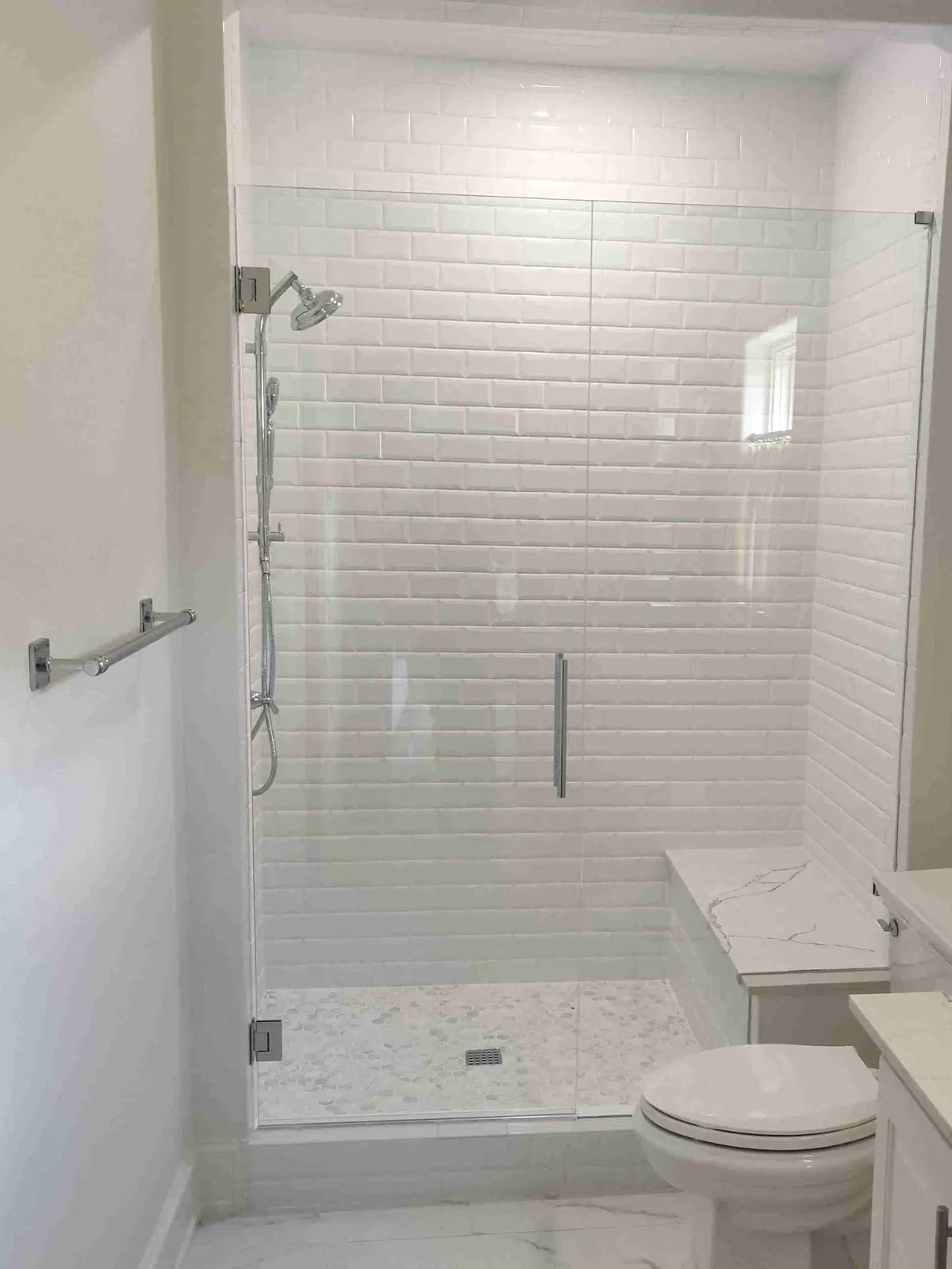 Frameless glass door and panel with a towel bar across a white subway-tile shower