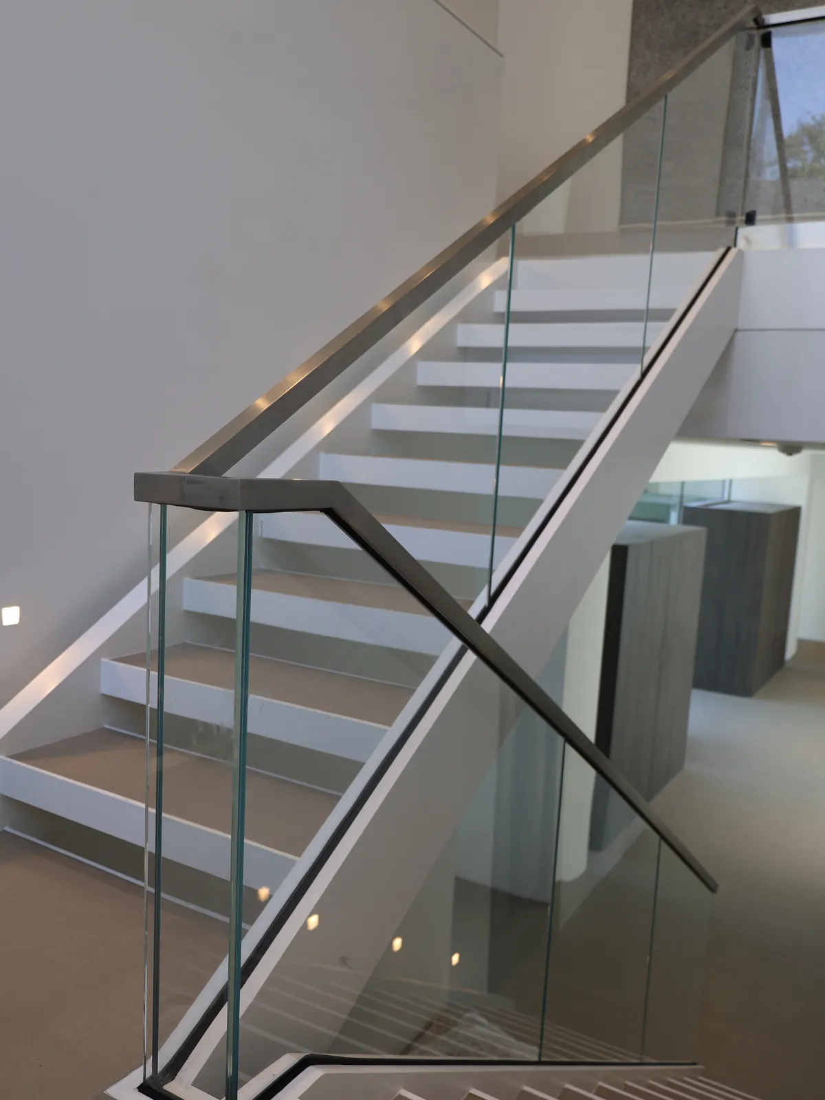 Glass stair railing with a metal handrail along a switchback staircase