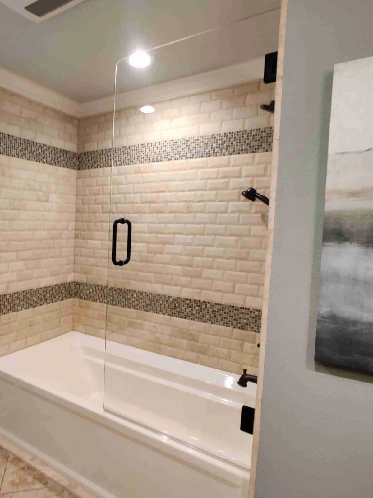Single glass door on a bathtub with a matte black pull and beige subway tile