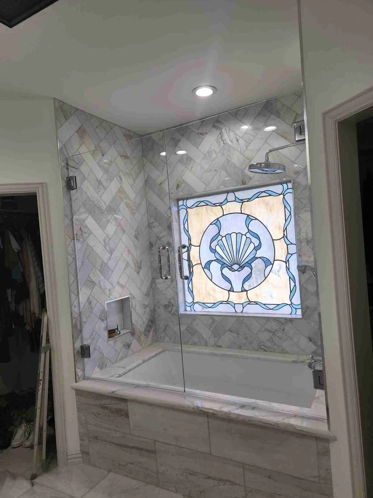 Glass tub enclosure with a hinged door beneath a stained-glass window and herringbone tile