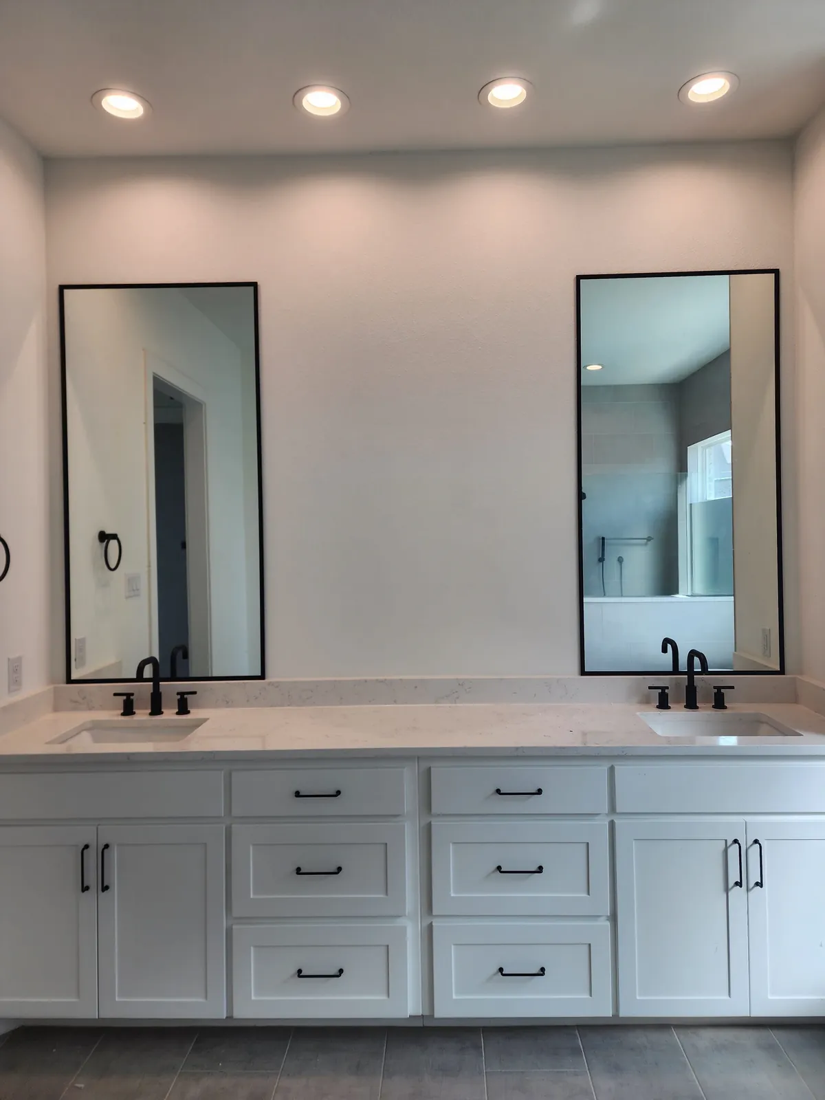 Two tall black-framed mirrors above a double vanity with matte black faucets