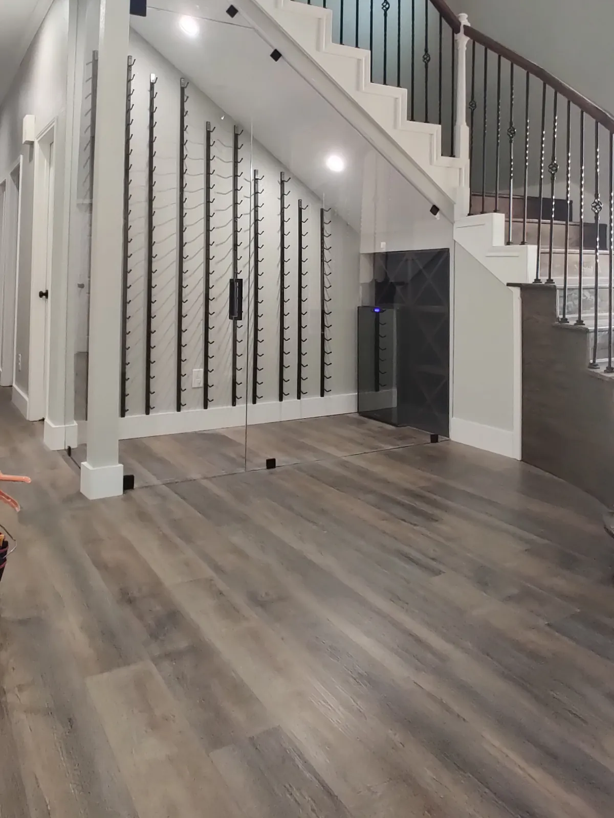 Glass wine cellar enclosure under a staircase, with wall-mounted bottle racks