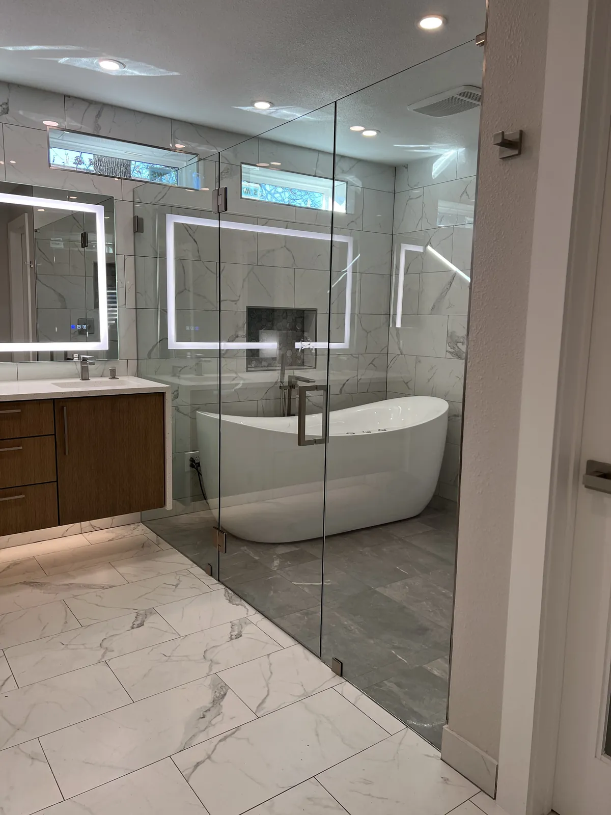Floor-to-ceiling glass wall with a door, enclosing a wet room with a freestanding tub