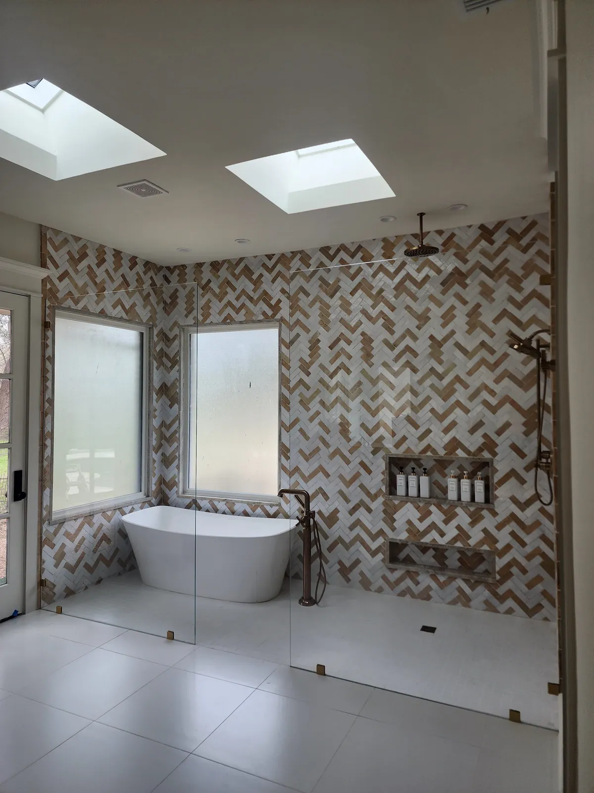 Fixed glass panel enclosing a walk-in wet room with a freestanding tub, herringbone tile and brass fixtures