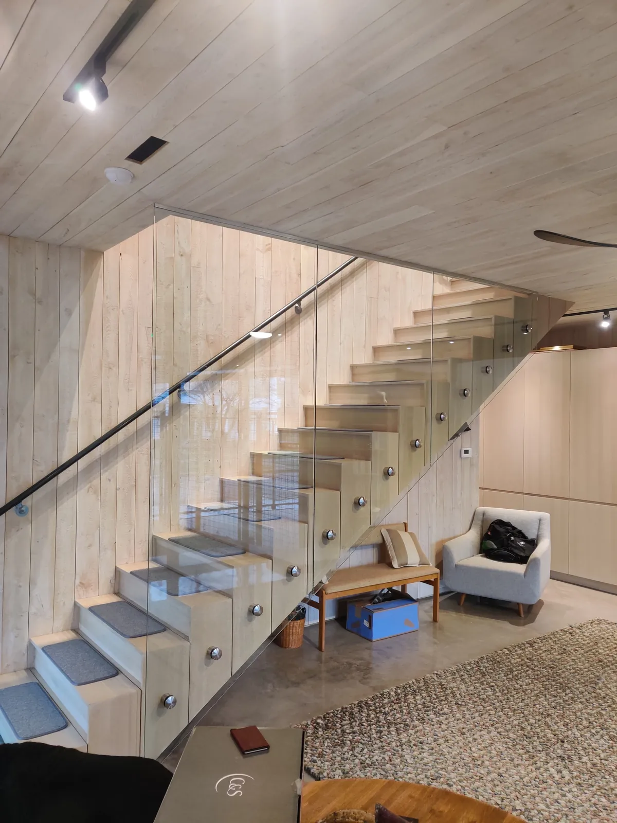 Frameless glass stair guard with a black handrail beside a wood-clad wall